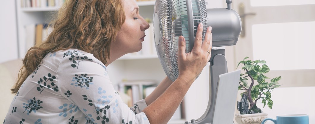 Woman cooling down with fan sat at desk